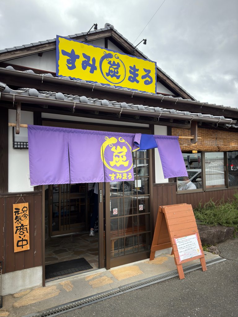佐賀県武雄市北方町にある炭火焼すみまるの店舗外観。黄色と青の大きな看板と紫色の暖簾が目印になっているお店
