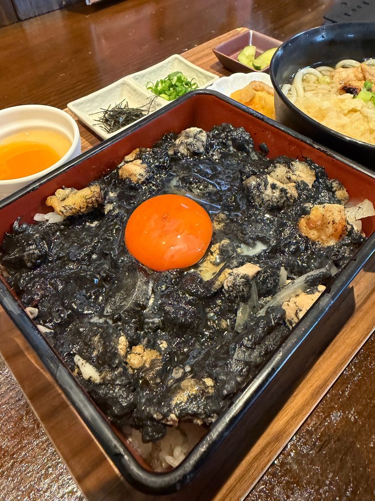 すみまるの黒い親子丼と平日ランチセット。真っ黒な親子丼にオレンジ色の卵黄がのり、ミニうどんや小鉢も付いたボリューム満点のランチ